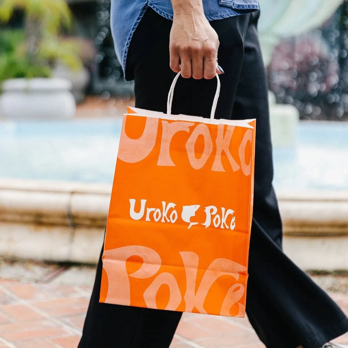 Person holding an Uroko Poke branded orange takeout bag outdoors
