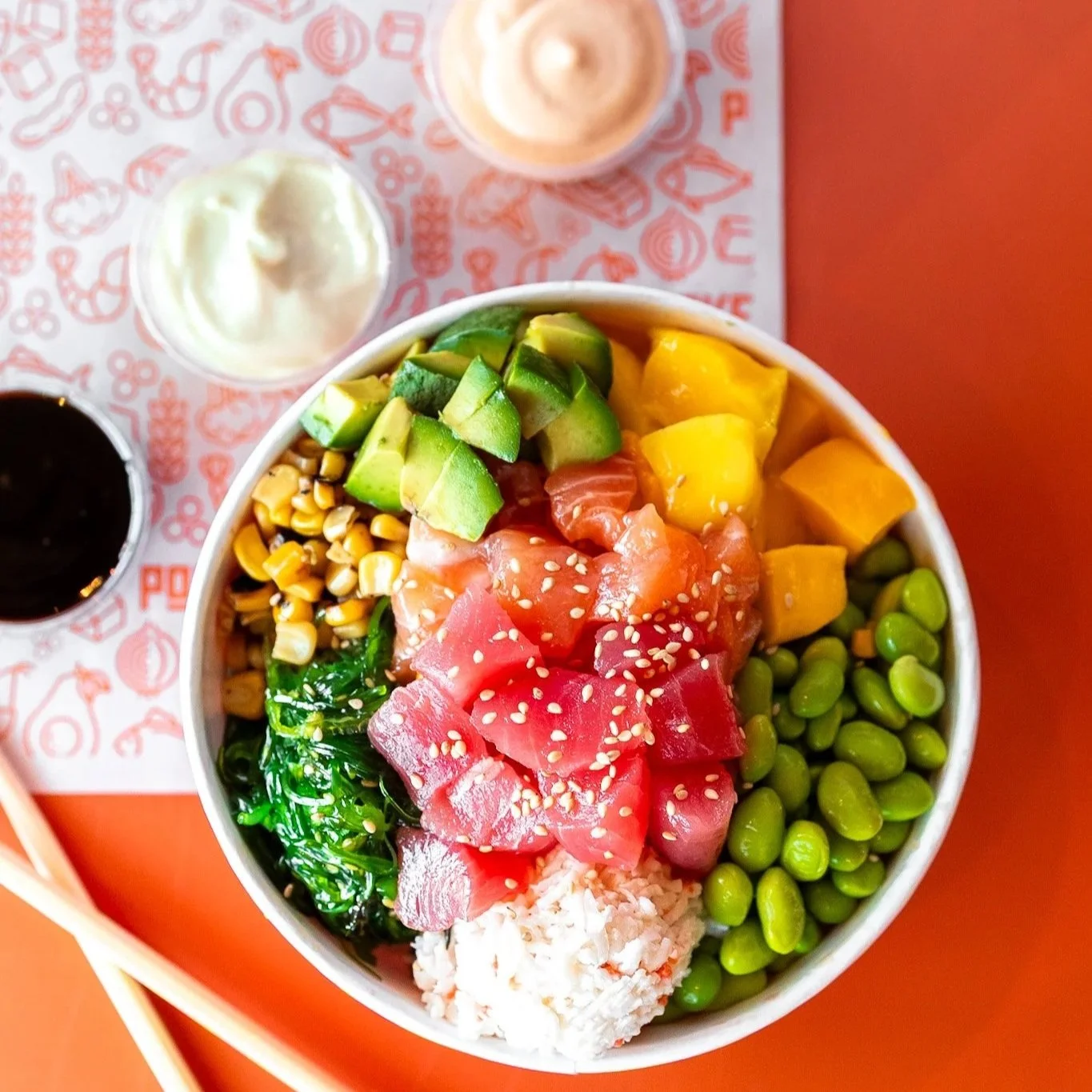 Fresh tuna poke bowl with edamame, cucumber, mango and sesame on an orange background