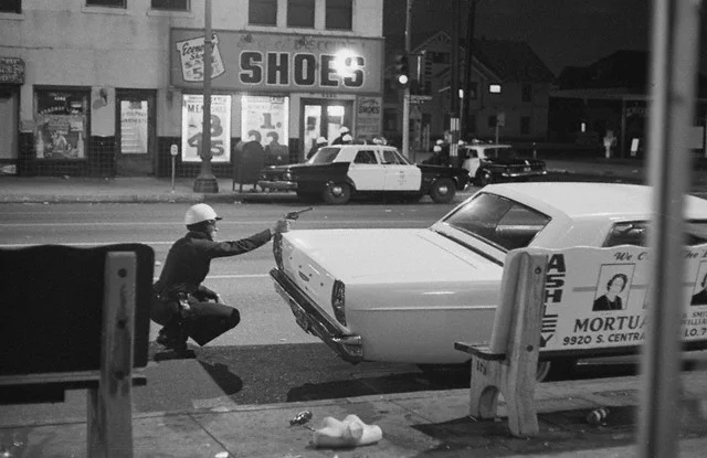 Move In On Sniper. a policeman aims his revolver at building from which a sniper was taking potshots at passing cars during rioting early Aug. 15th in the Negro community of Watts. Across the street, fellow officers crouch behind cars as they move in closer. Moments later National Guardsmen arrived on the scene and reported they had hit the sniper with return fire. Bettmann/CORBIS (1965)