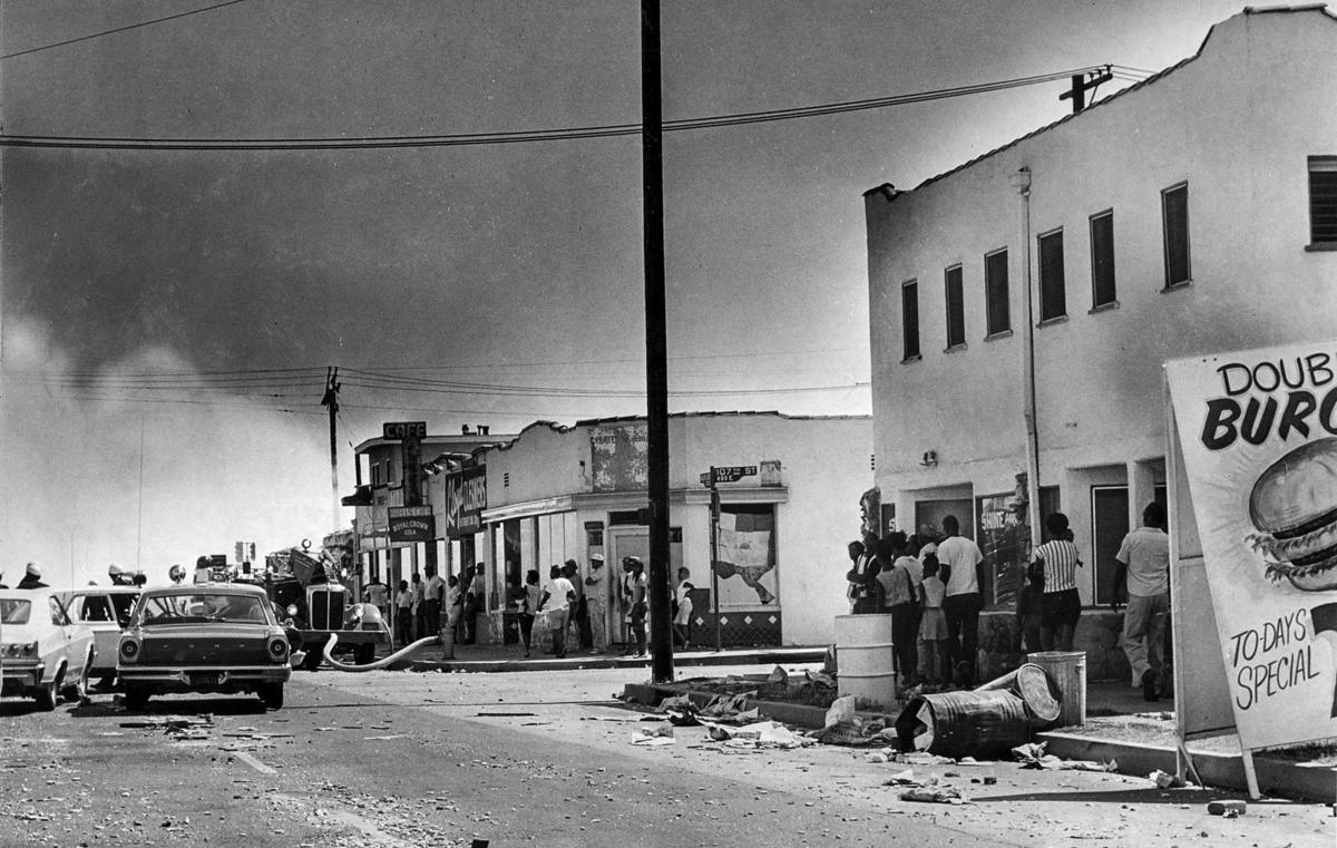 Debris litters Avalon Boulevard near 105th Street as pedestrians watch smoke rise from a building at 108th Street. (John Malmin / Los Angeles Times) 1965