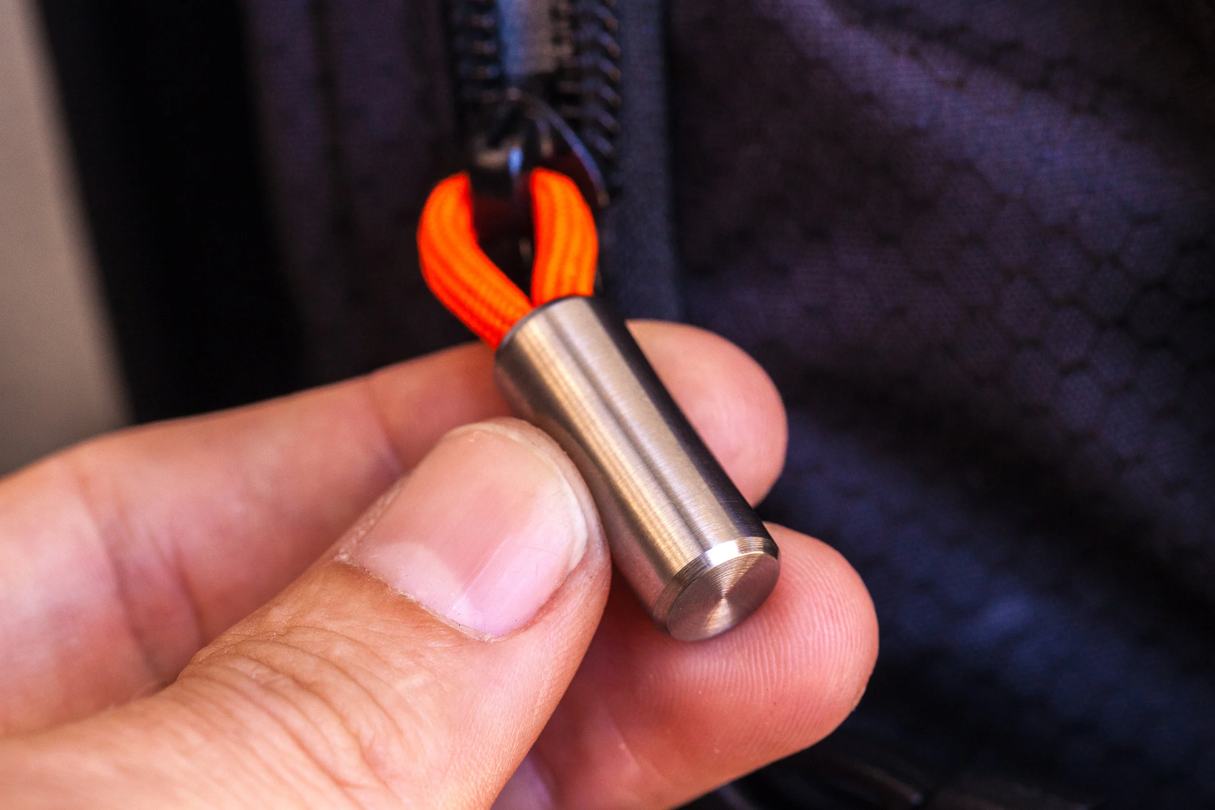 Round titanium Cord Lock with blaze orange 550 paracord used as a zipper pull on backpack.