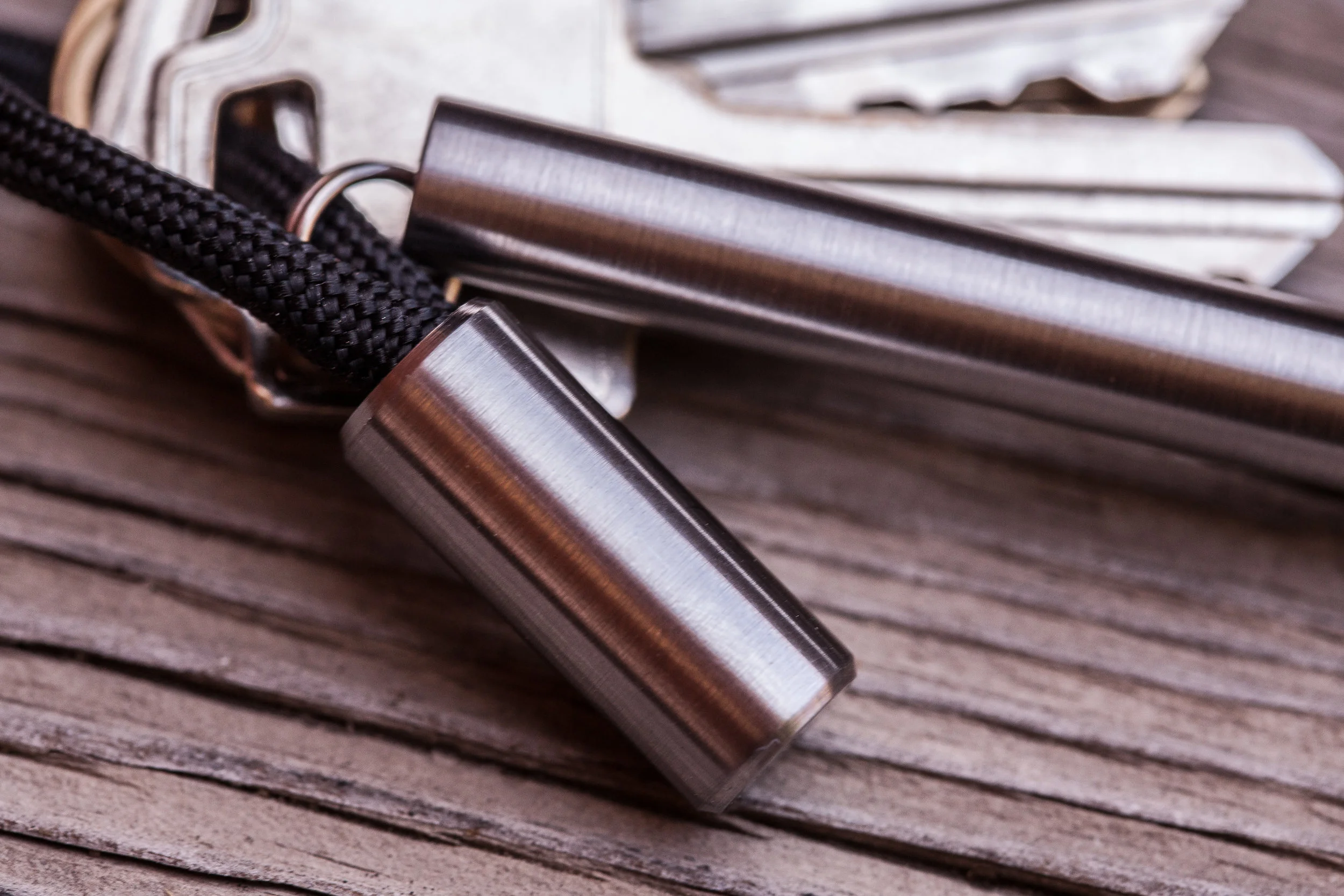 Close up detail showing the surface finish of the titanium Cord Lock with black 550 paracord next to the titanium EDC Ink keychain pen.