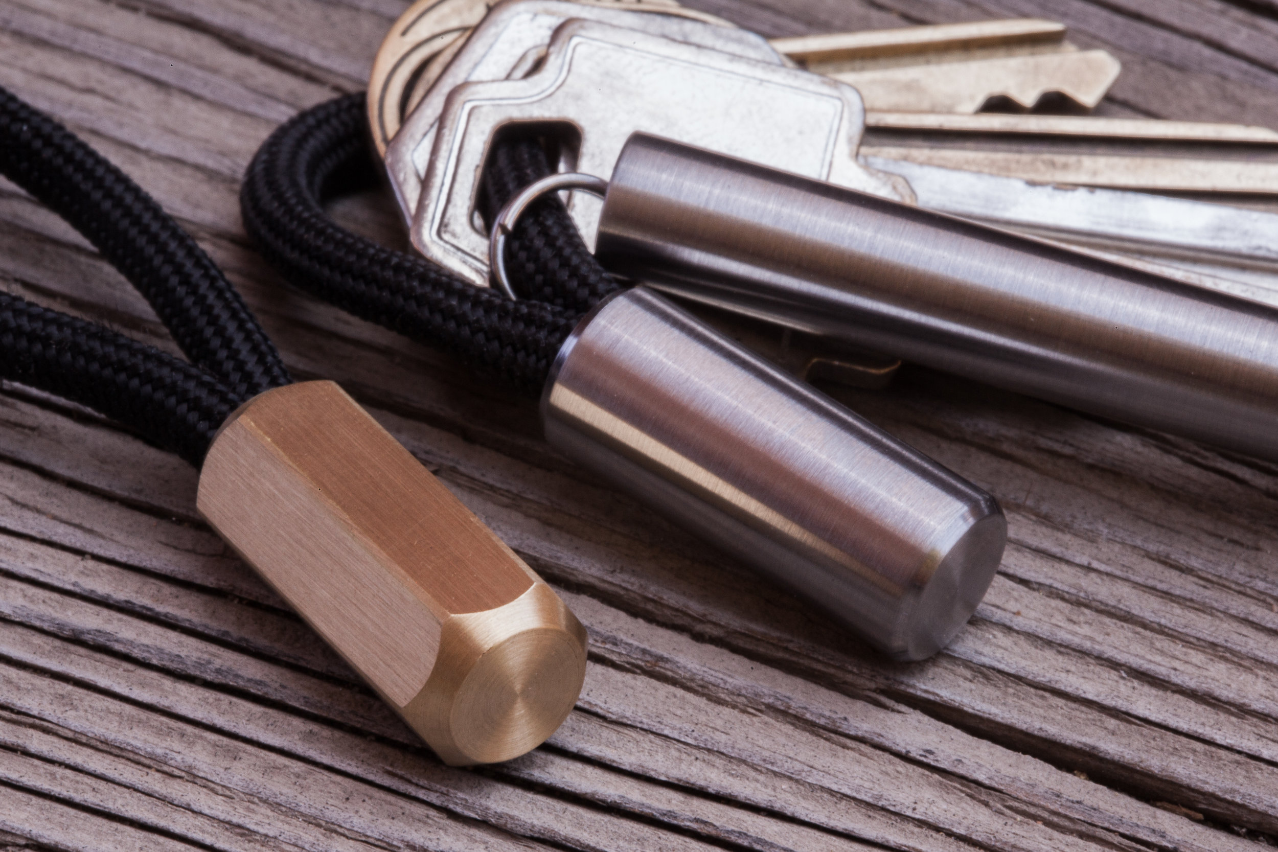 Close up detail of the round titanium Cord Lock, and the brass hex Cord Lock, shown next to the titanium EDC Ink keychain pen.