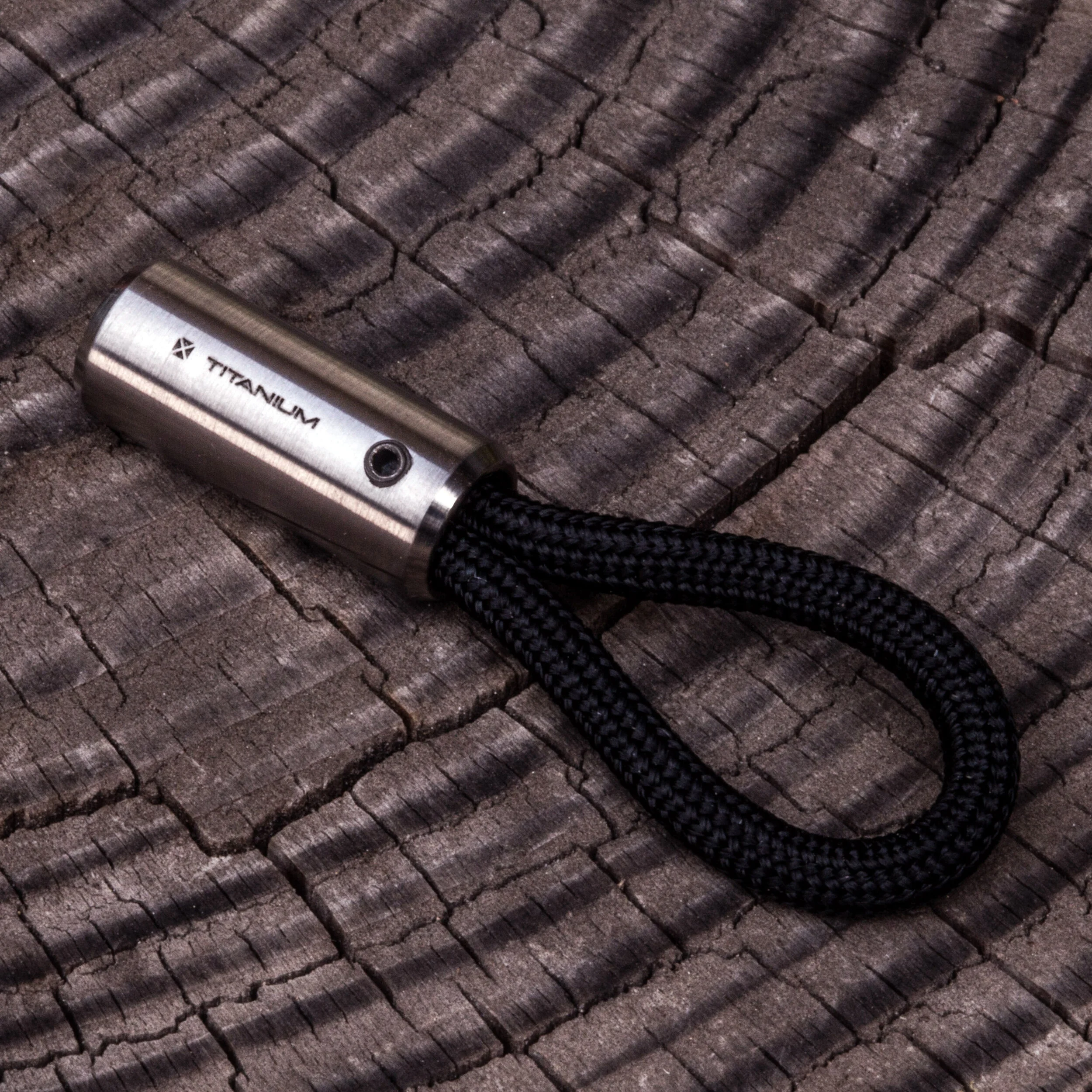 Round titanium Cord Lock with black 550 paracord showing the laser engraving of the word "titanium" and the BLANK FORCES logo.
