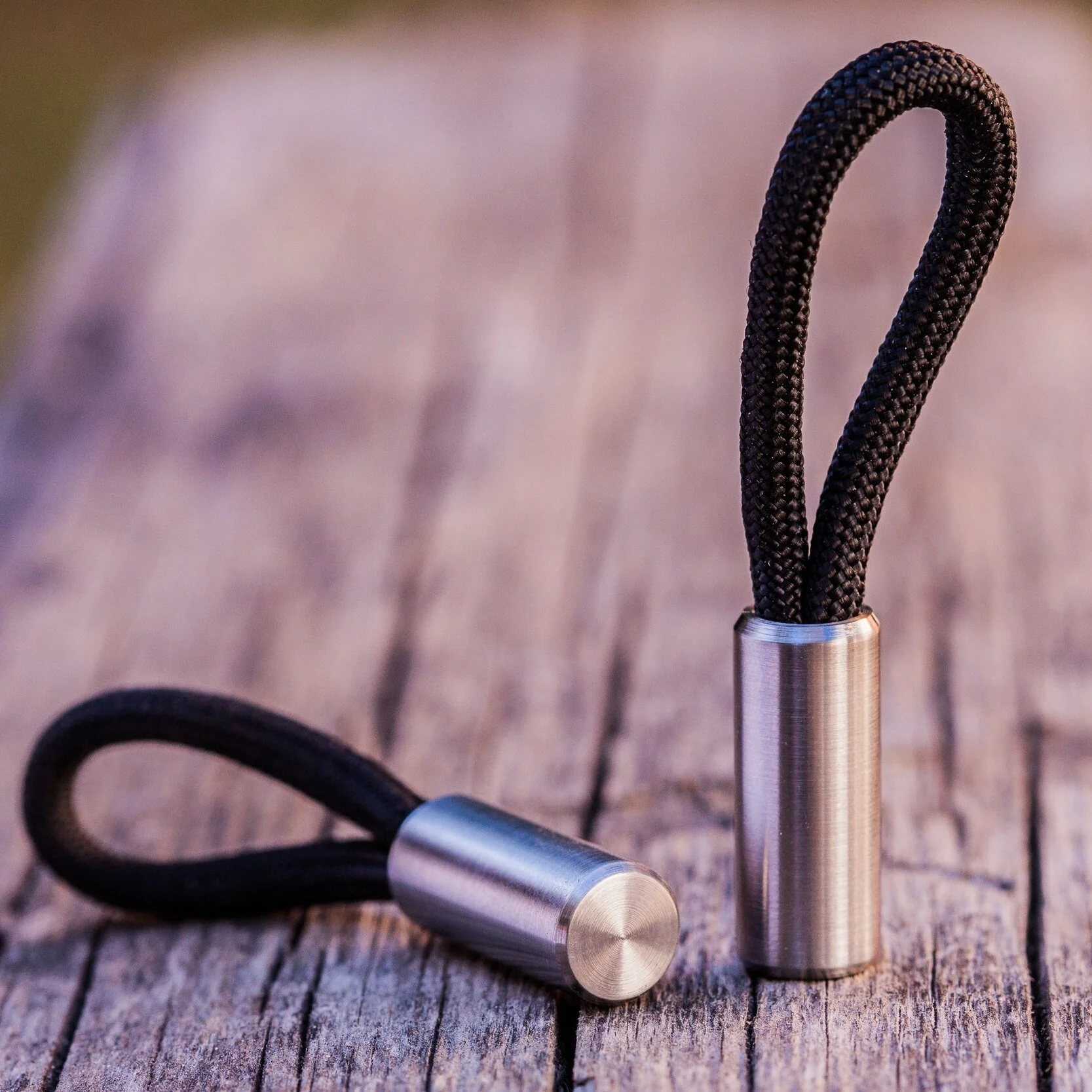 Round titanium Cord Locks with black 550 paracord one standing vertically, one laying down on table.