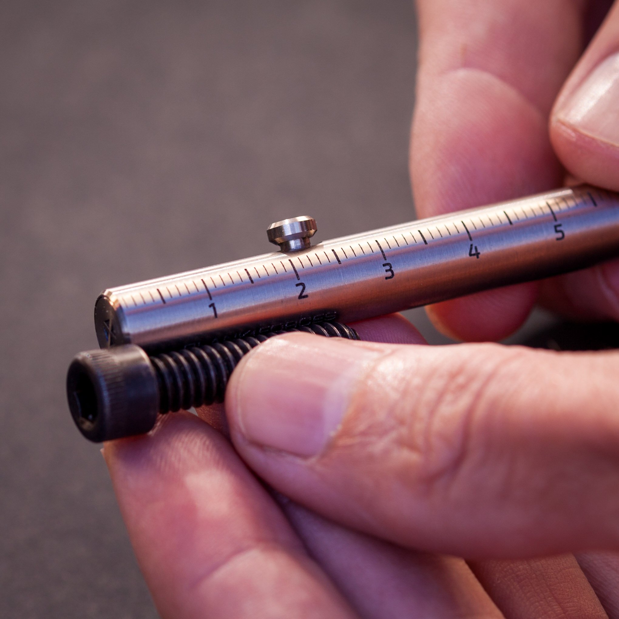 Closeup measuring a screw with the PRO version of the Injector titanium bolt action pen.