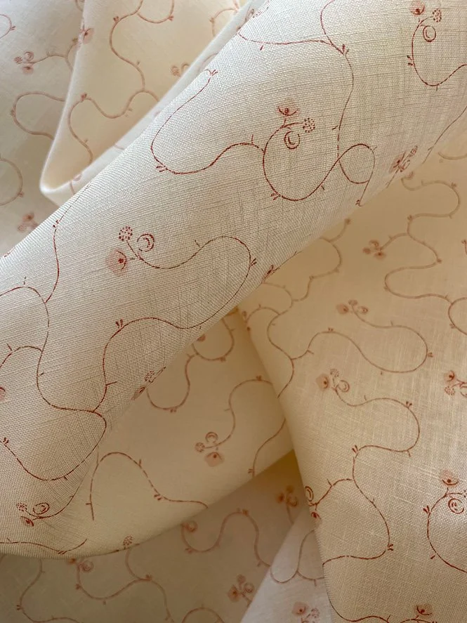 Parlour Posy Russet on Antique Cream midweight linen pooled in soft folds, emphasising drape and small floral design.