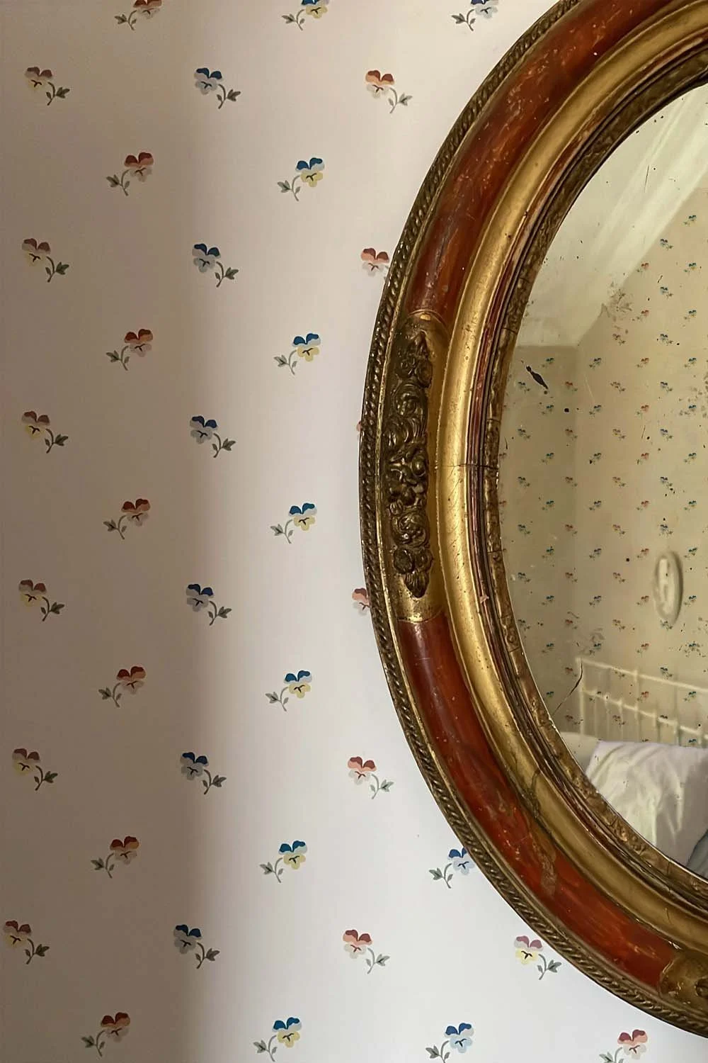 Antique mirror reflecting soft light against English country floral wallpaper with multicoloured pansies.