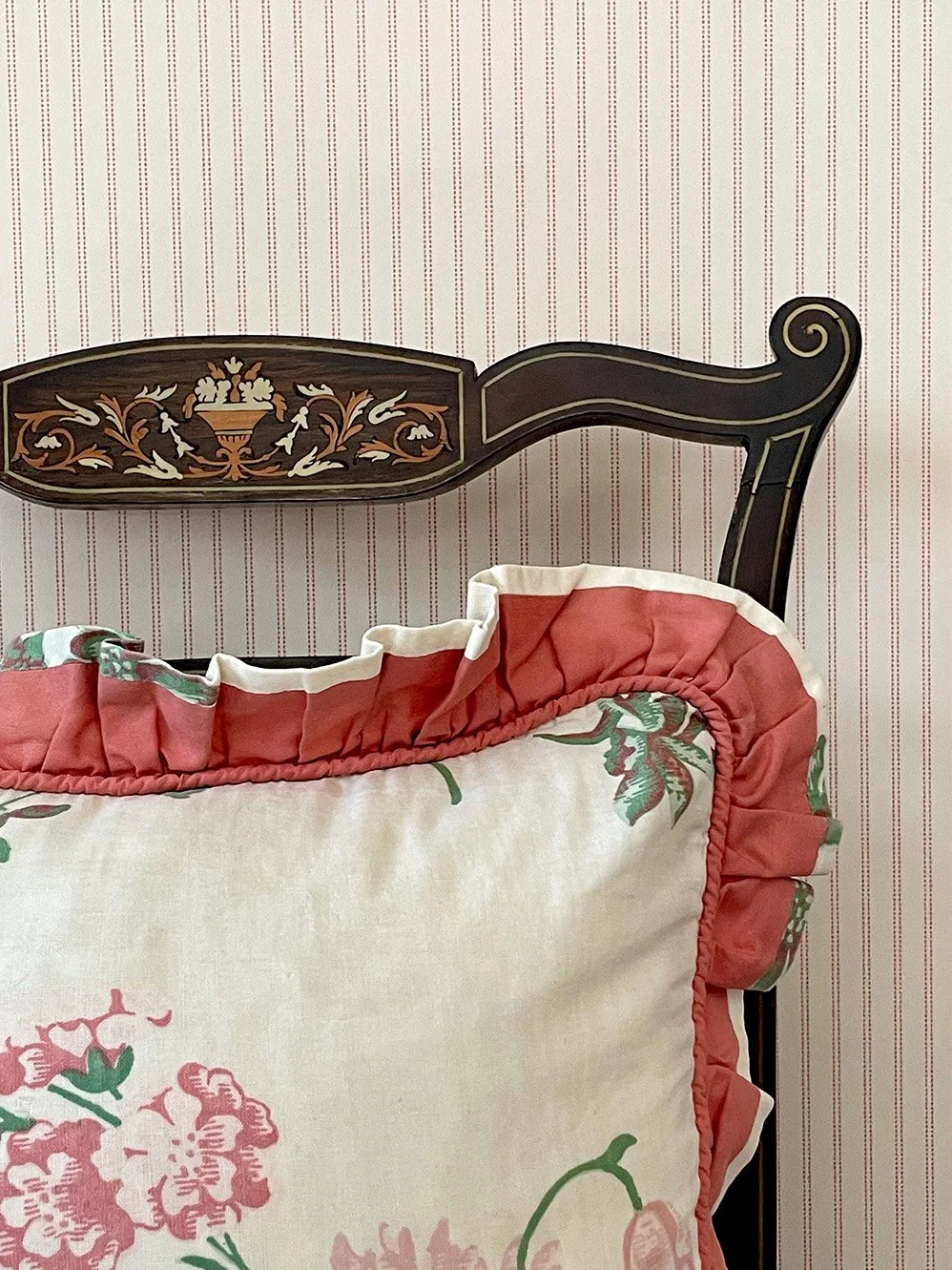 Pillow Stripe Marsala Pink wallpaper sample behind antique chair and ruffled floral cushion.