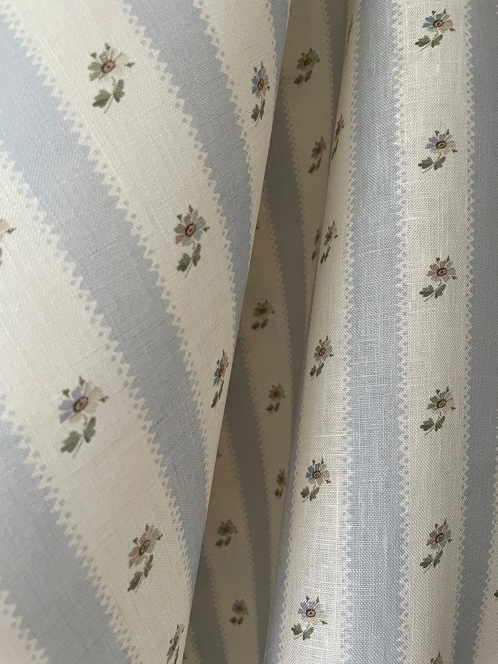 Hat Box Stripe Pale Blue midweight linen fabric close-up showing pale blue candy stripes and small daisy sprigs.