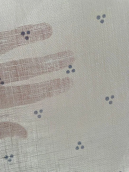 Petite Trio of Dots Faded Blue held with hand behind to reveal light filtering through.