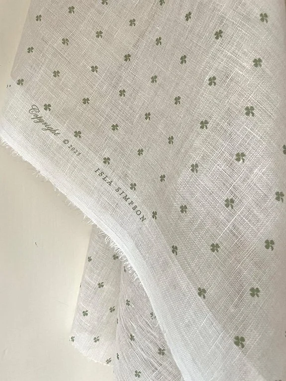 Close-up of Cottage Clover sheer linen fabric in Lichen green, showing pattern and branded fabric legend on selvedge edge.