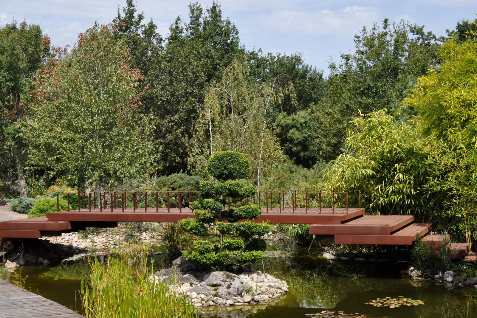 Japanese-inspired modern corten steel bridge over pond by José António Andrade