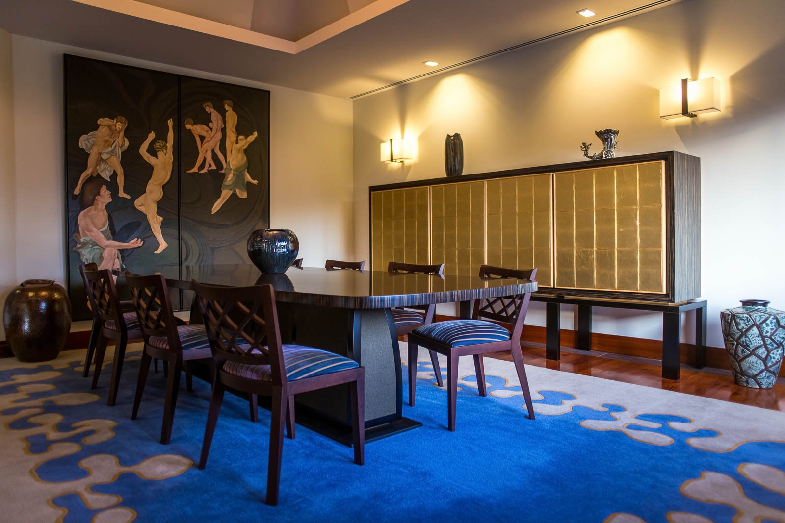 Sala de jantar sofisticada em tons de dourado e azul, com mobiliário de autor, aparador folheado a ouro e, ao fundo, pintura a óleo original