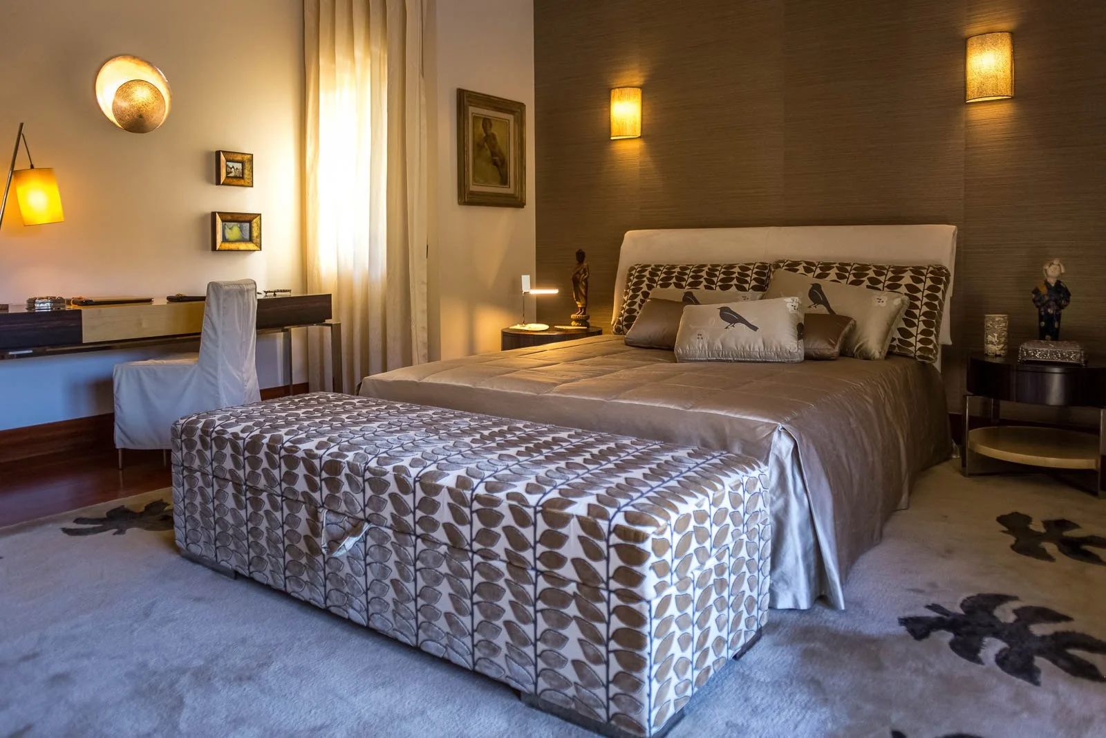 Quarto luxuoso em tons claros e dourados, com mobiliário de autor e têxteis em cetim com padrões bordados