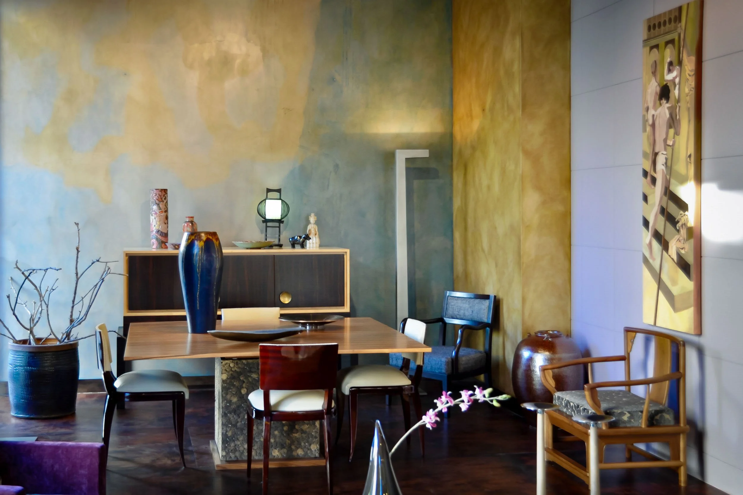 Dining area detail at the showroom of José António Andrade interior design studio in Porto, Portugal, showcasing an elegant custom-designed table, designer chairs, and a trompe-l’oeil wall painting as the backdrop.