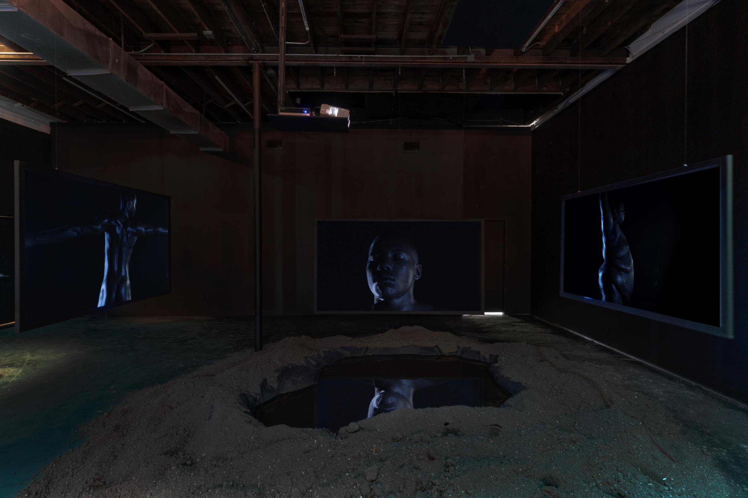  ‘The Language Must Not Sweat’ (2019).   Five-channel video projection, soil, sound, haint-blue lights, water 