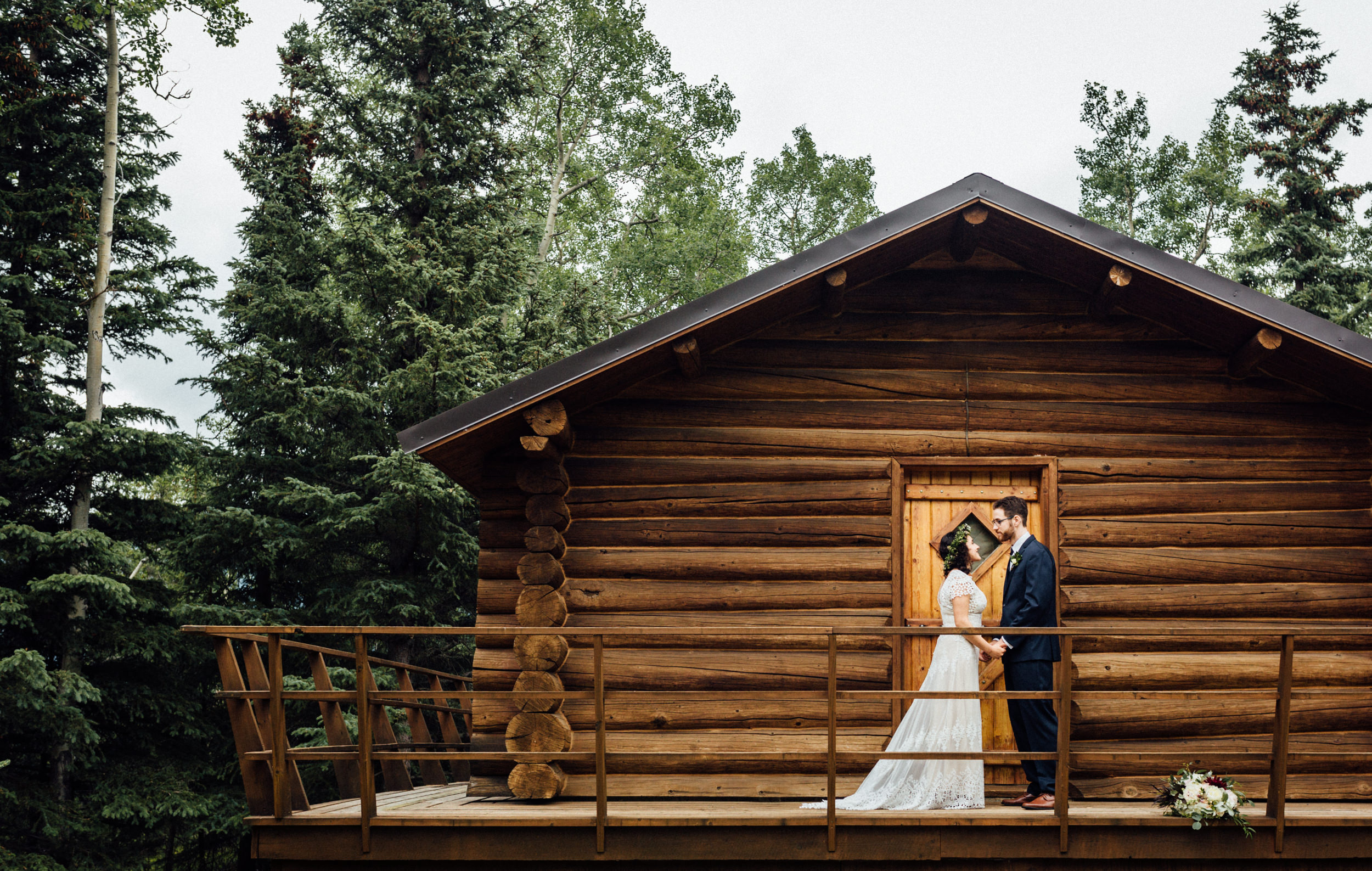 Couple holding hands in front of Alaskan log cabin 