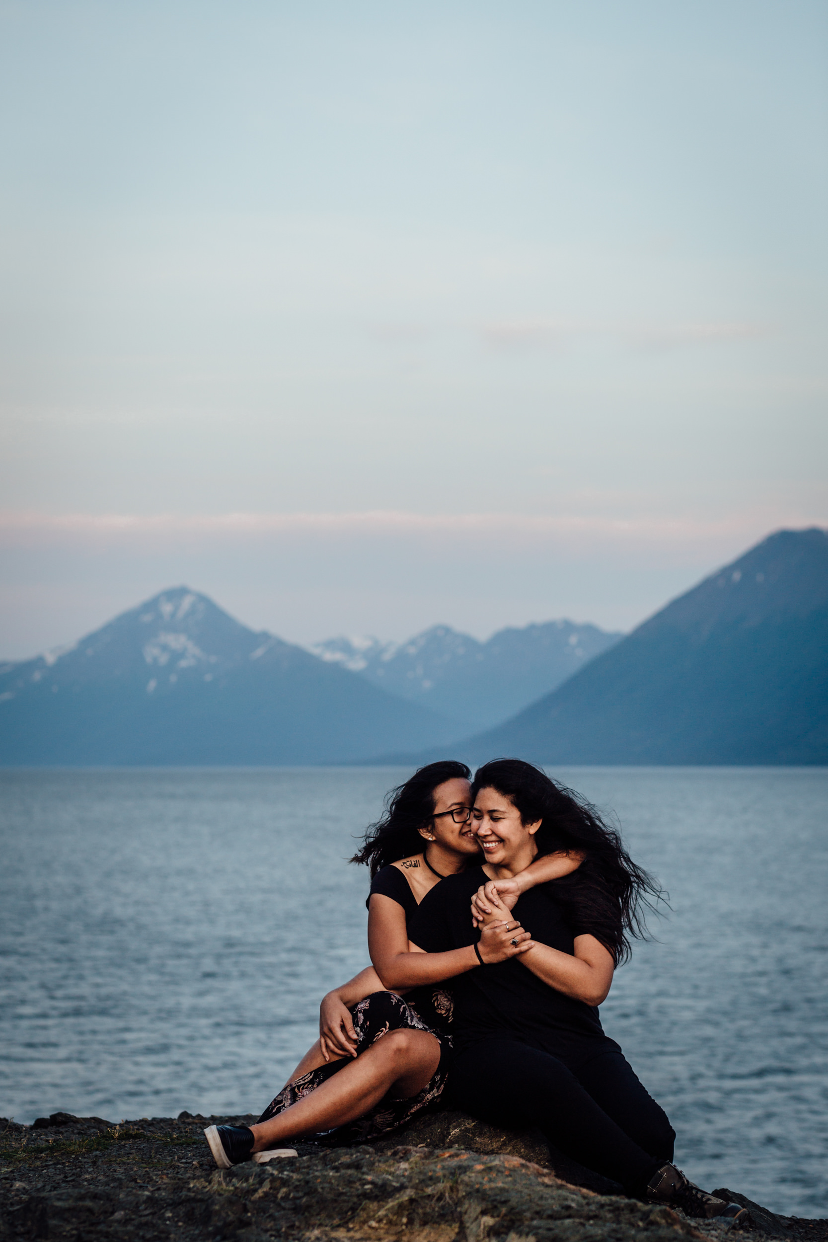 Couple snuggling in front of water and mountains