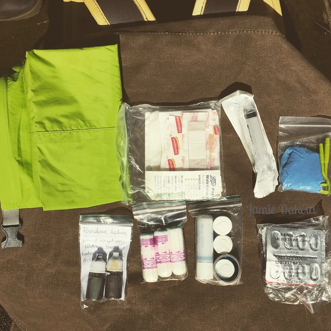 A backpack with a green jacket, a green bag, and various other items arranged neatly on a surface.