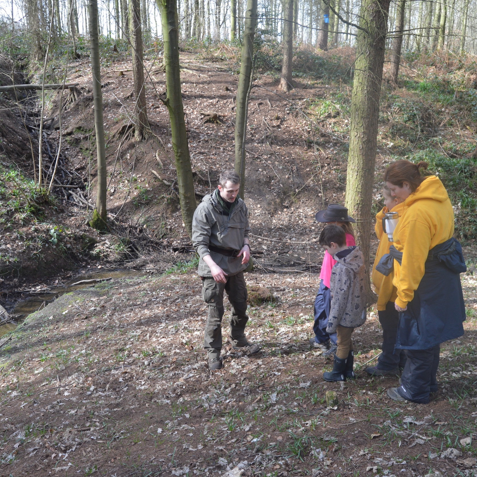 A man and two children stand together in a lush green forest, surrounded by tall trees and dappled sunlight.