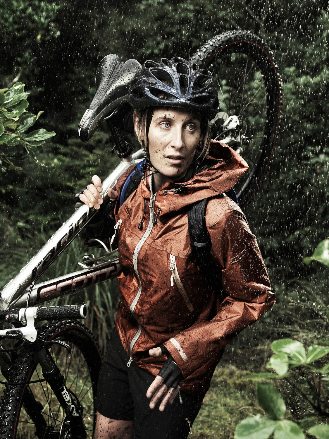 Woman carrying mountain bike through bush in the rain