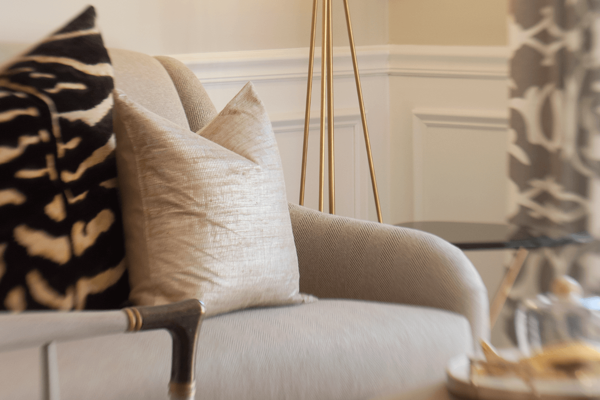 Close-up of a beige upholstered sofa with throw pillows, one with a zebra print pattern, in a well-lit living room with wall paneling and a gold floor lamp.