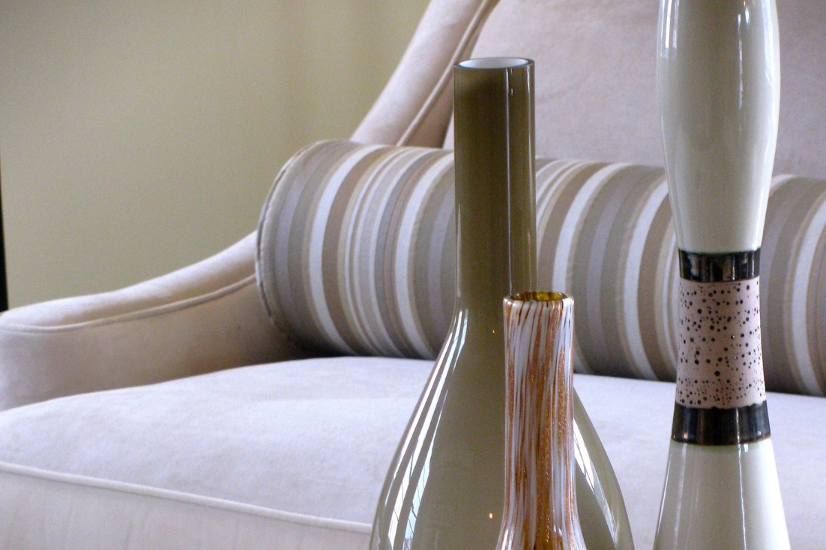 Close-up of three decorative vases on a cream-colored sofa with striped and solid patterns in a living room setting.