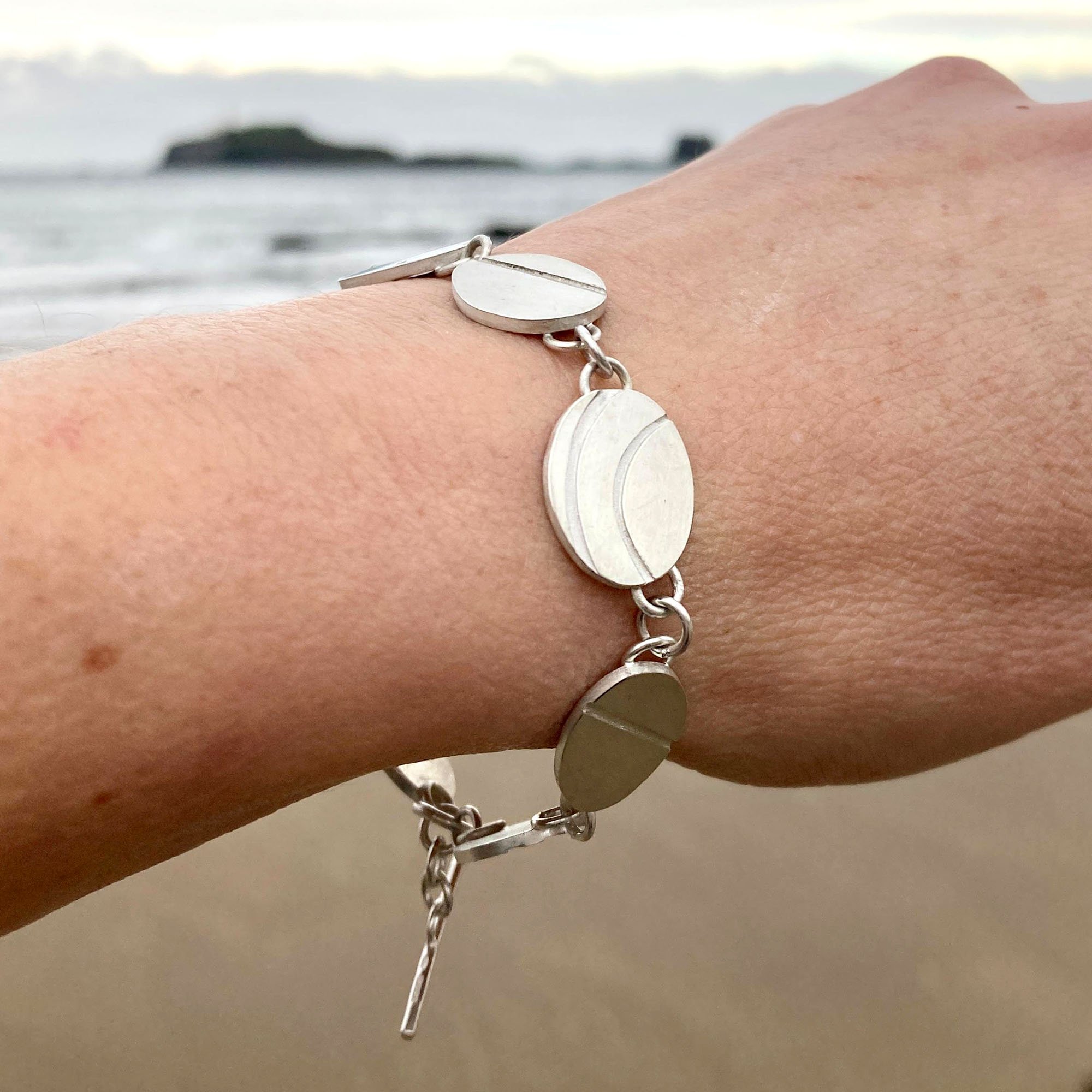 Close-up of a handmade silver pebble bracelet worn on the wrist, inspired by Cornish beach stones with natural quartz lines, showcasing its delicate, recycled sterling silver charms.