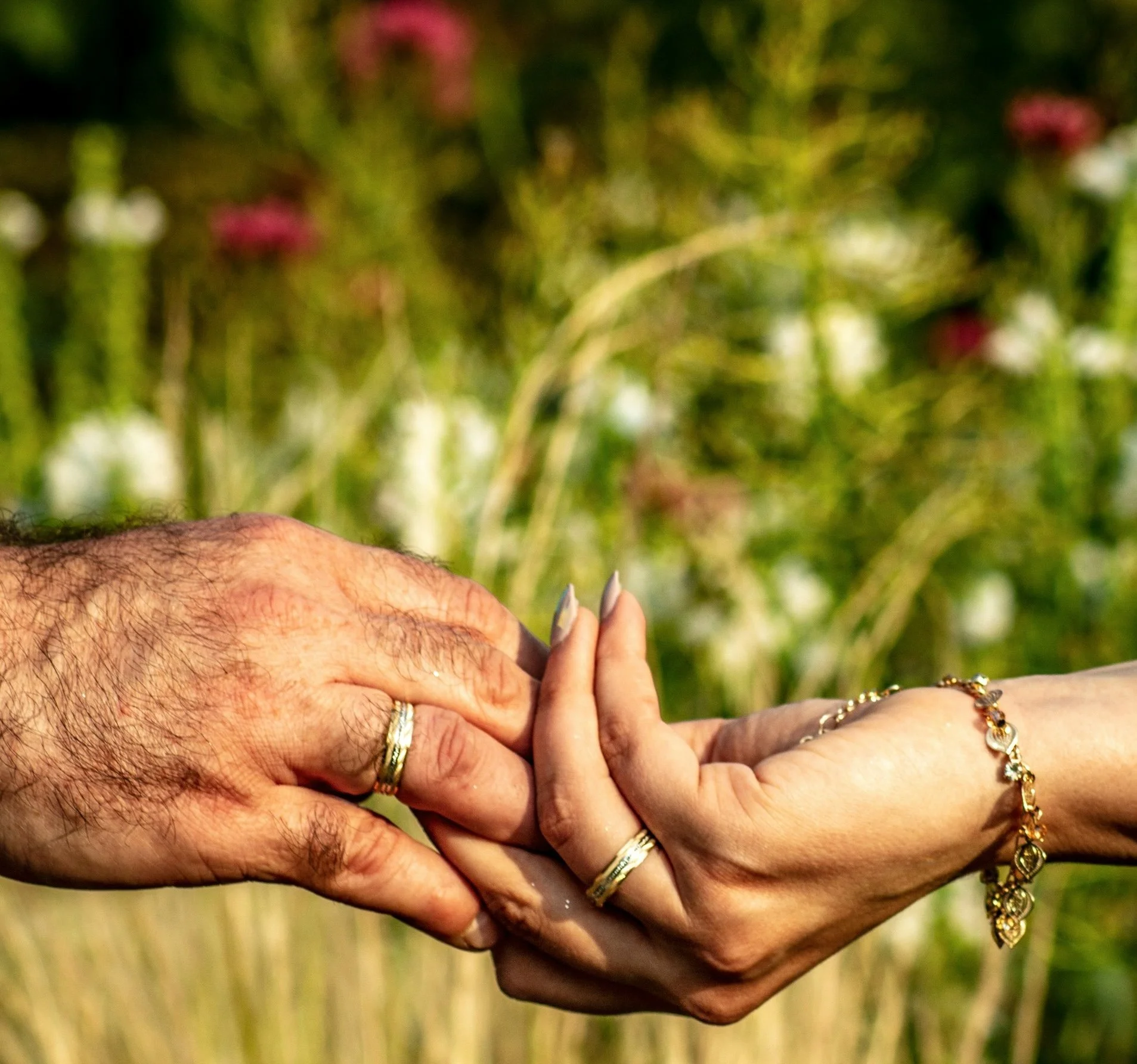 A man and woman's hands, held together in a garden.