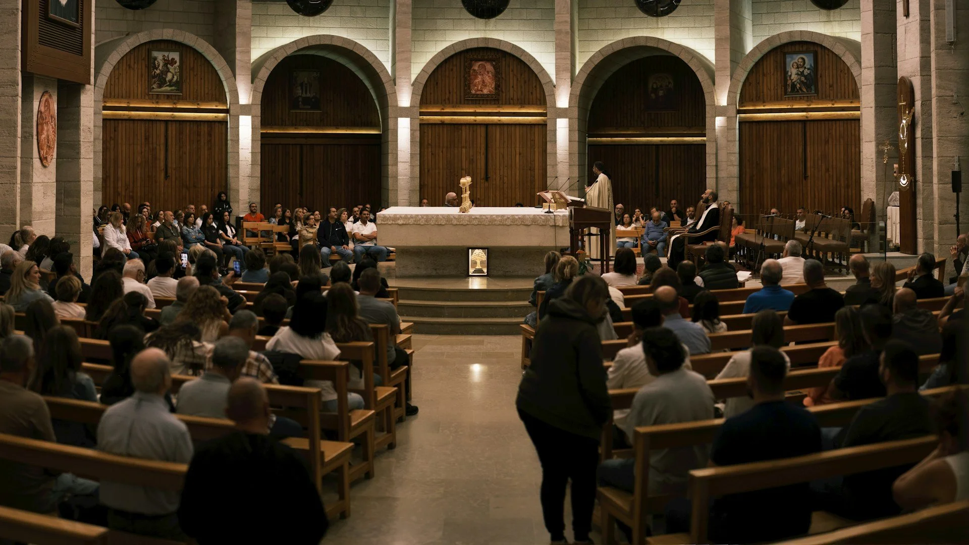 A group of people in wooden pews in an old, formal church setting.