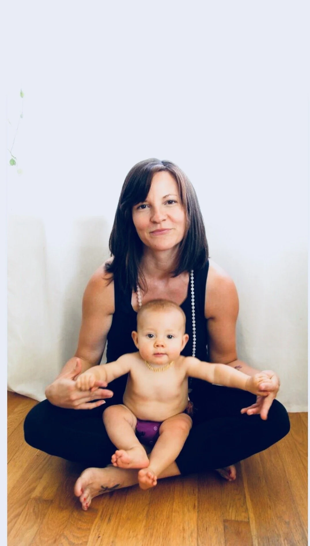 Jess, a certified Postpartum Doula, Prenatal and Postpartum yoga instructor and Hypnobabies® Birth Educator, smiles with baby in lap.