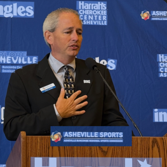 Chris Smith, President of the Asheville Buncombe Regional Sports Commission gives a speech while holding his hand over his heart, symbolizing the meaningful connection between the Asheville Community and Sports.