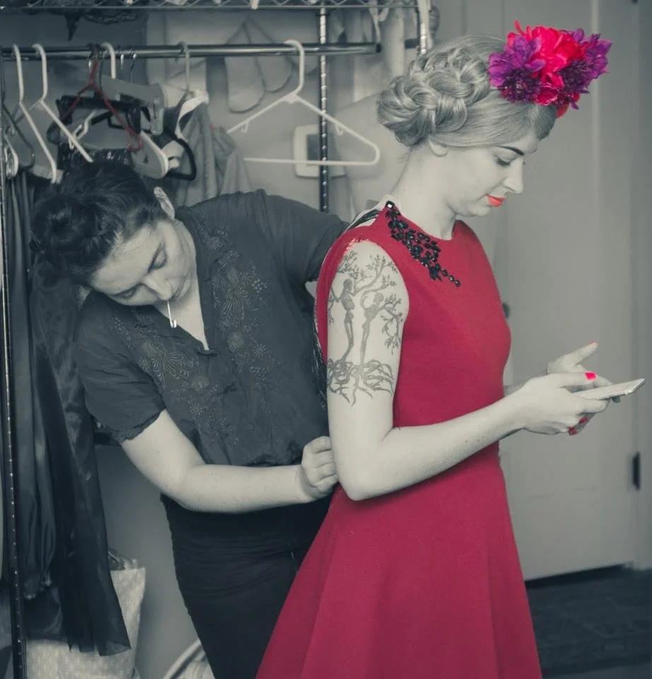 A woman fitting and sewing a dress onto another woman.
