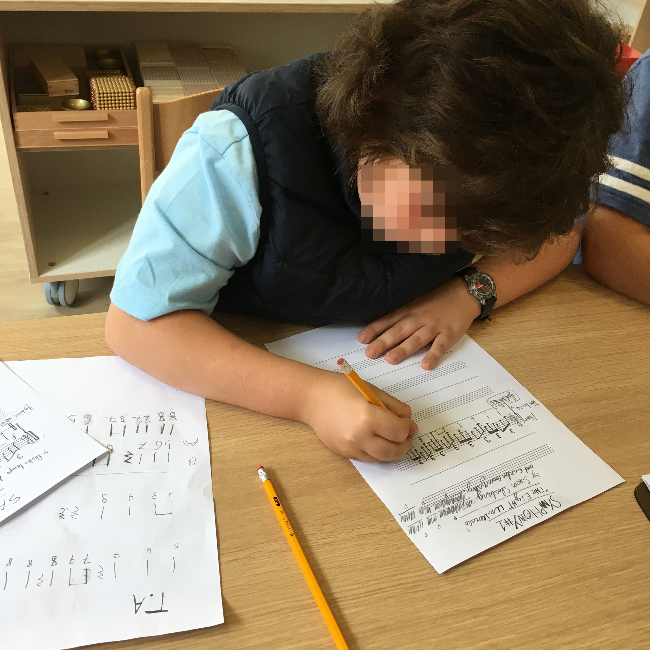 Christopher copies his themes onto the working draft. He writes his melodies on a one-line staff, just below Sully’s. Notice his stick-notated melodies on the paper to the left of the photograph. I like the way Christopher meticulously labelled his …