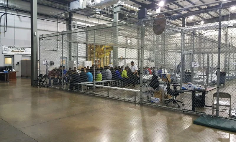 Children are being kept in large cages with chain link walls and concrete floors.