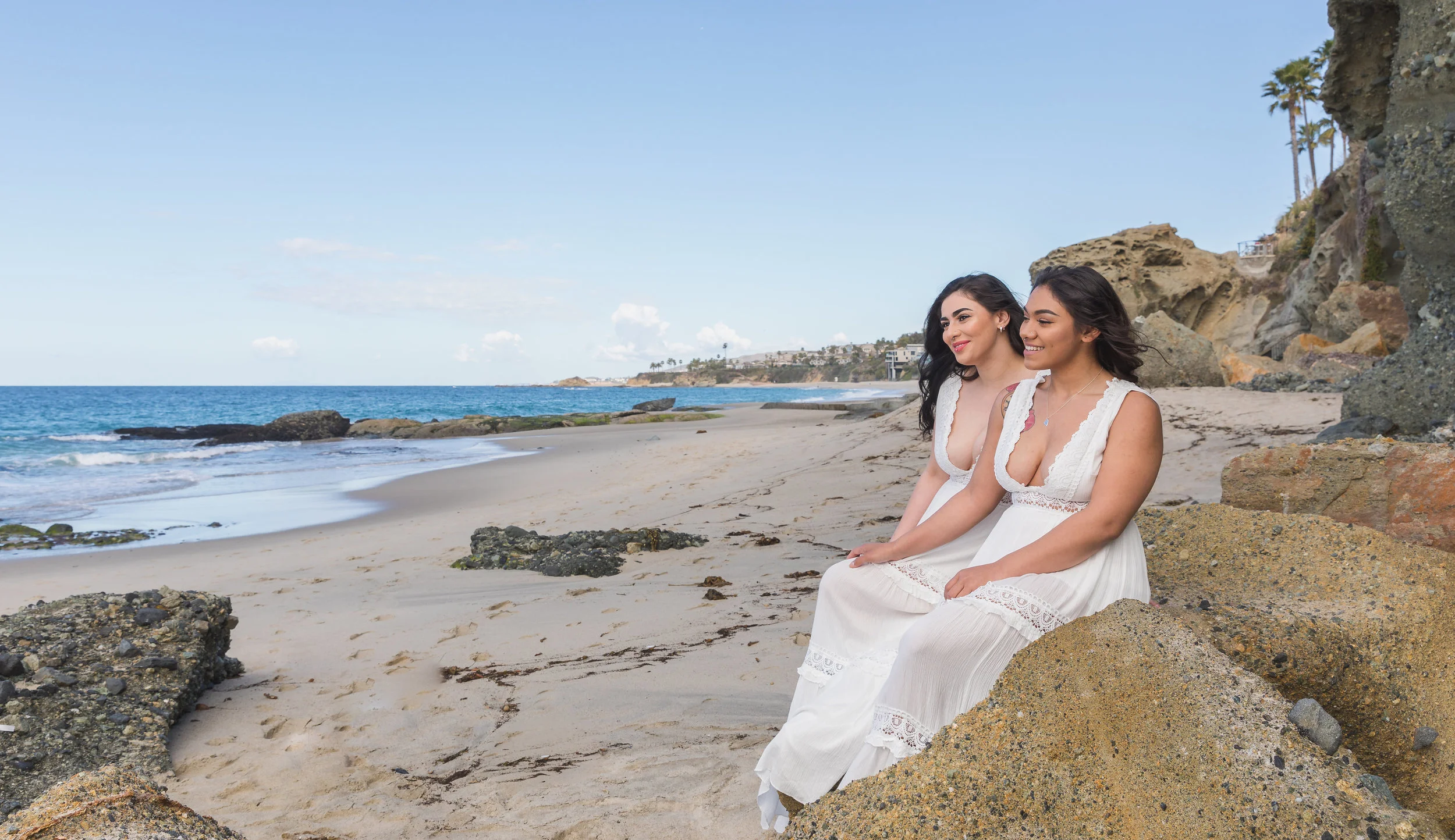 Two Women in White Dress Sitting on the Beach for Engagement Photo Session.jpg