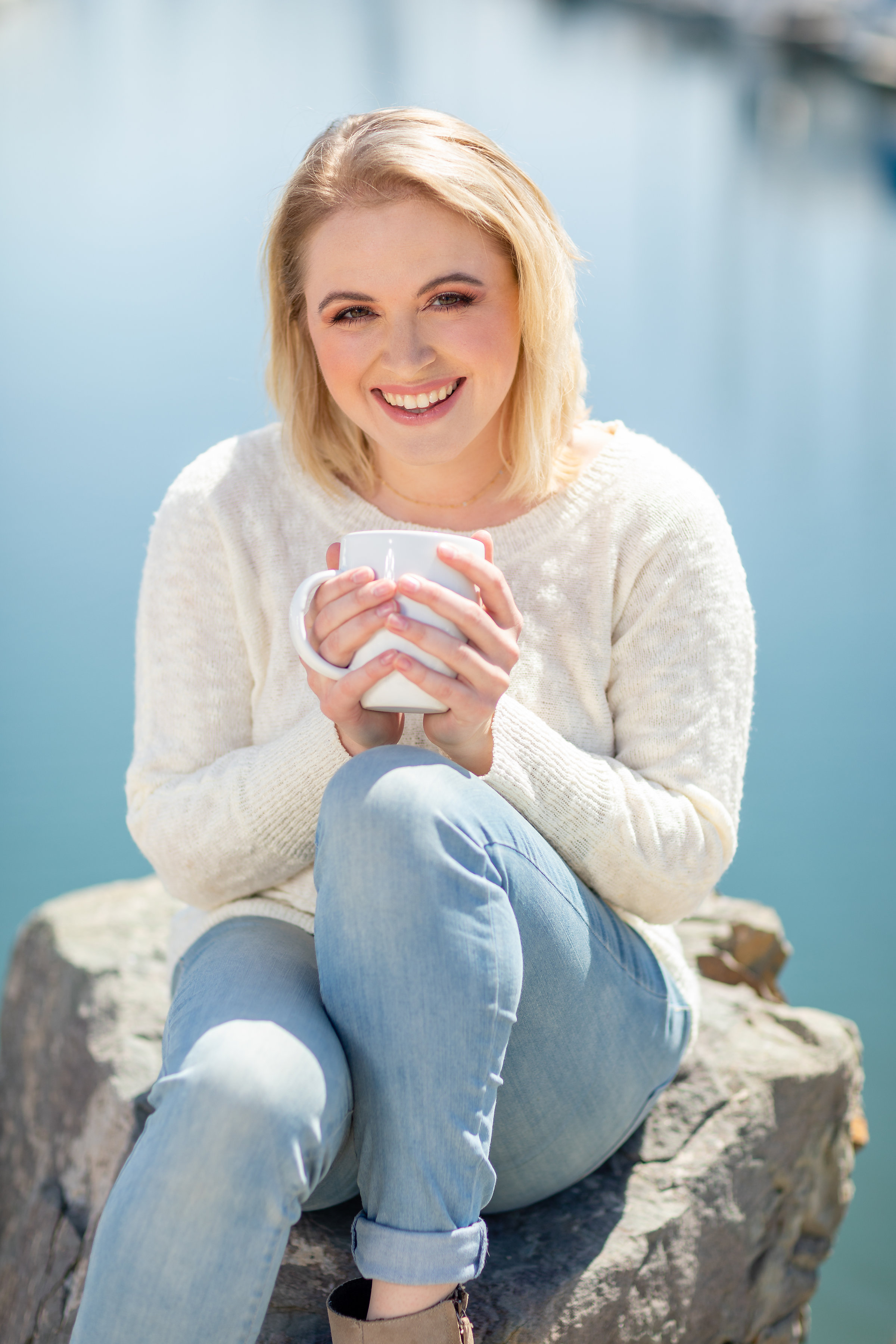 Female blonde in white sweater sitting on the rocks with coffee.jpg