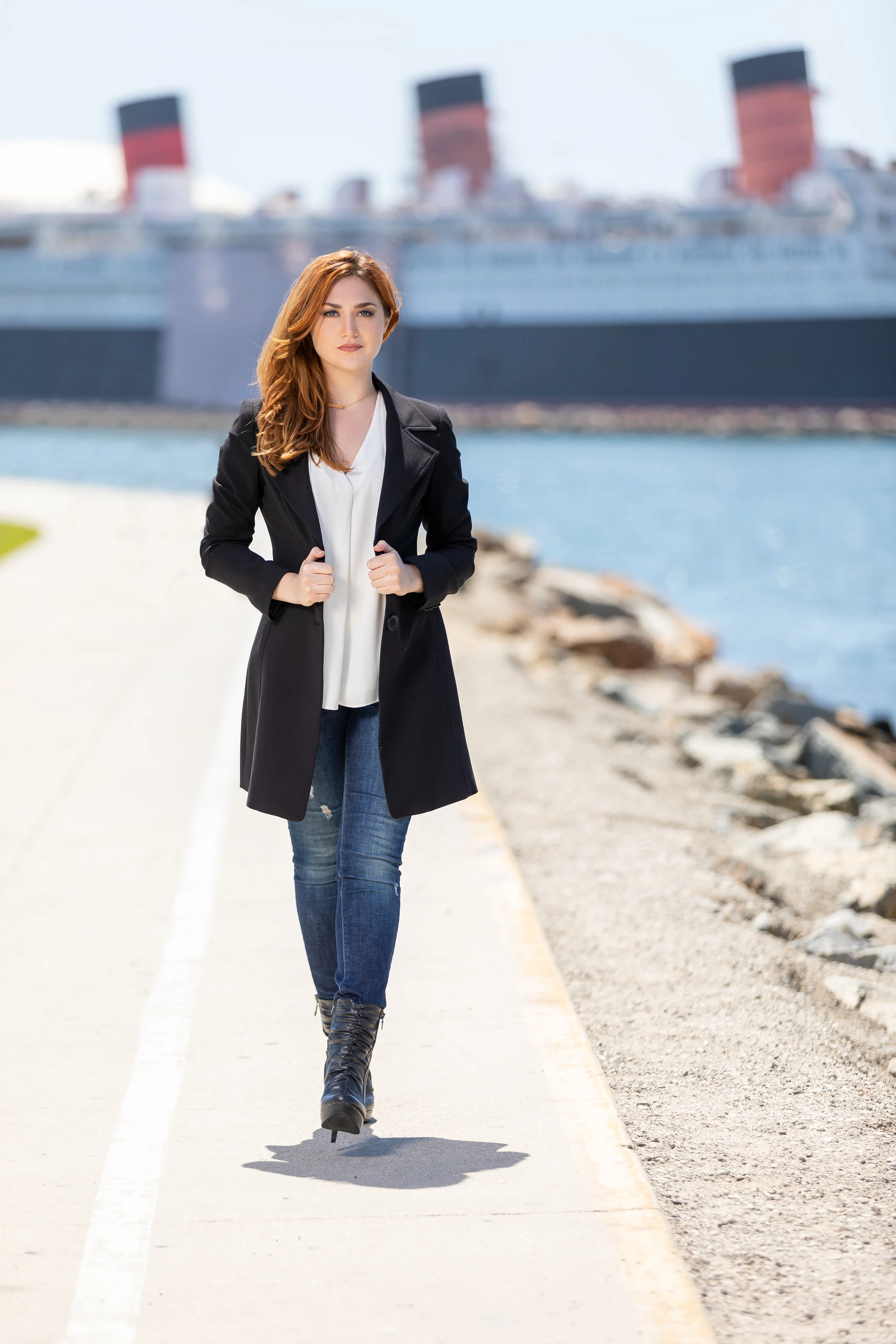High Fashion woman walking along the harbor in a long black jacket jeans and heeled boots.jpg