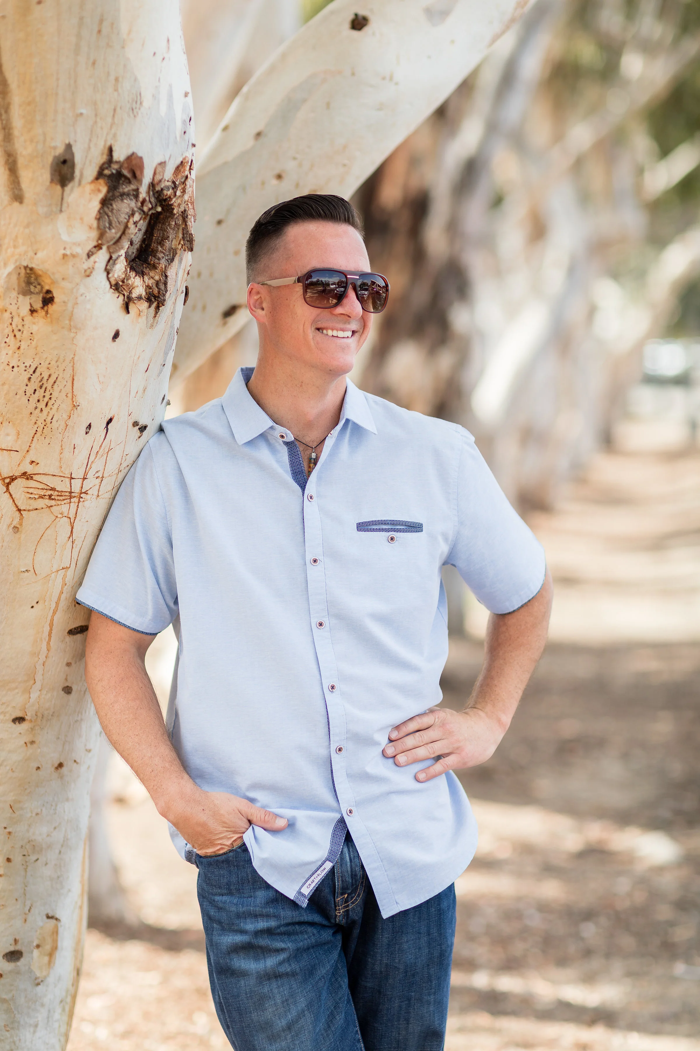 HB portrait of adult male standing by tree with sunglasses and a blue shirt.jpg