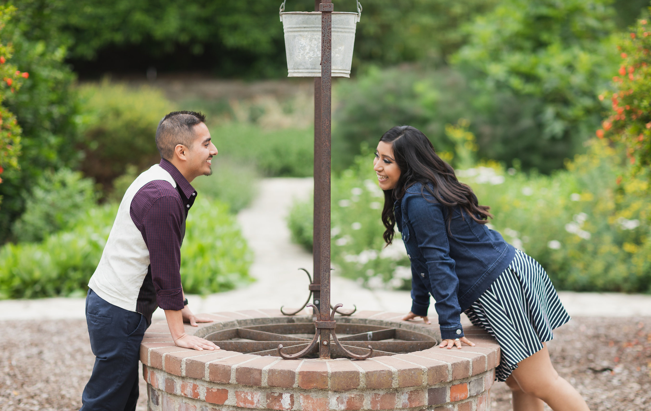Engaged couple smile over a wishing well.jpg