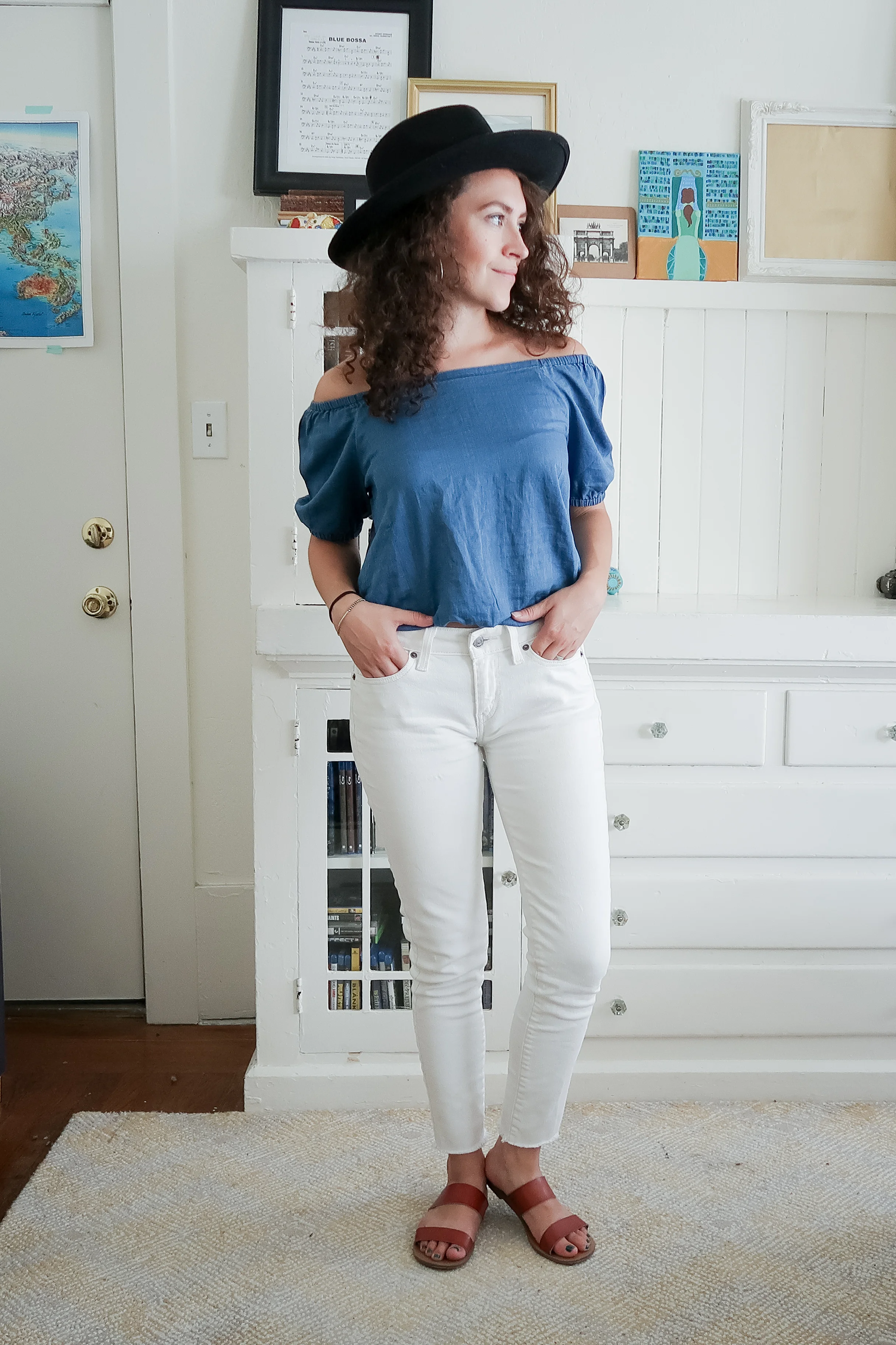 10 pieces, 10 outfits -- white levis skinny jeans worn with a bright indigo off the shoulder top from madewell, brown leather slide sandals and a black hat