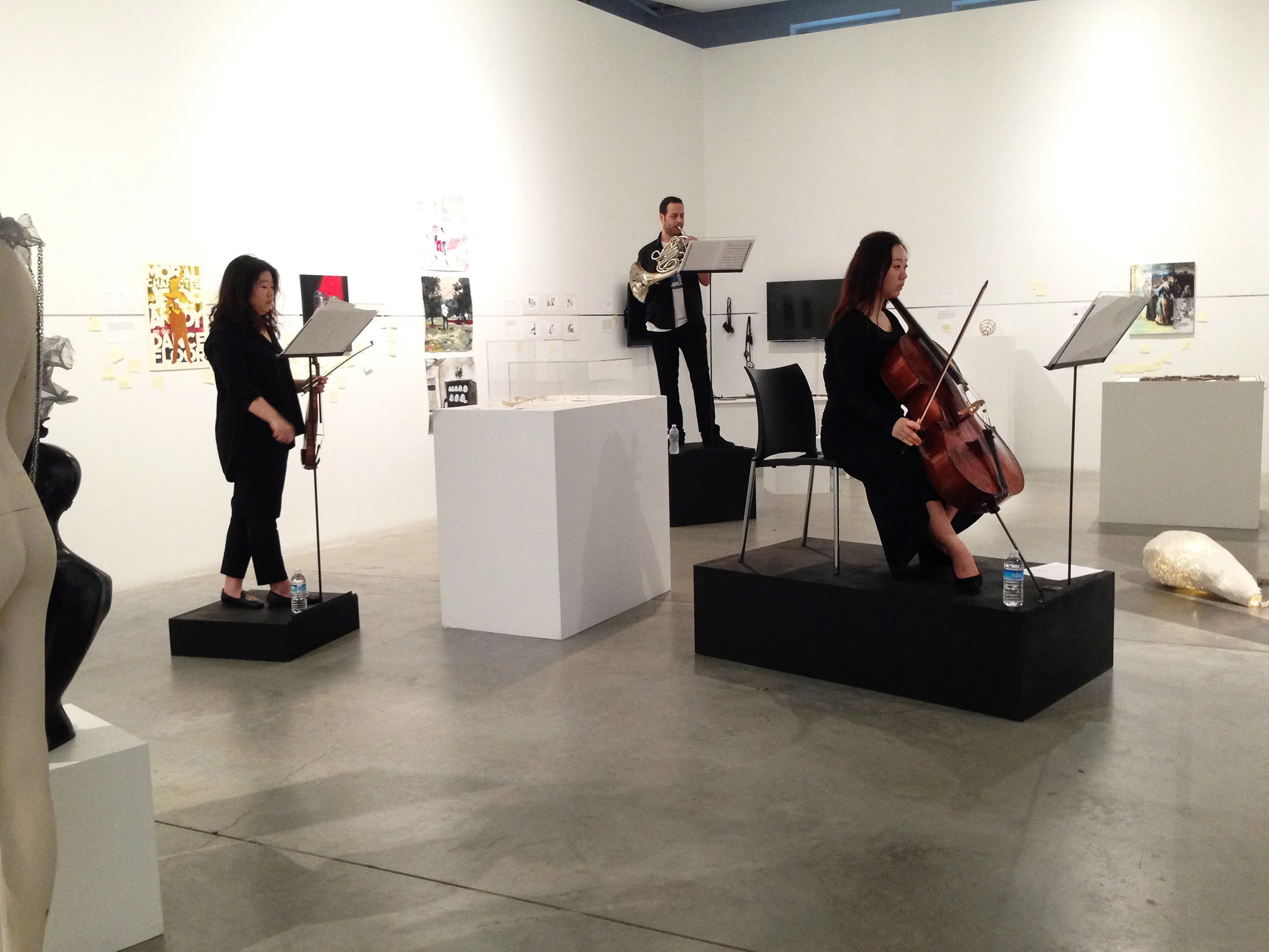 The partial view of the orchestra arrangement in the left wing of the gallery space. Each musician is standing on a black pedestal with fixed metal stand. The stands and pedestals vary in size. 