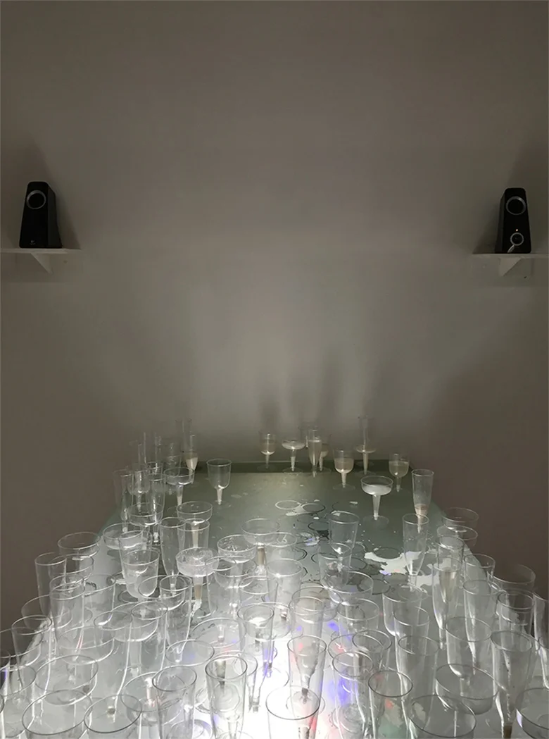  막걸리 (Makegeolli) is a traditional Korean rice wine, which is commonly served in a bowl. This installation allows for the audience to take makgeolli served in a martini and champagne glass. In the background, the two speakers are installed apart on t