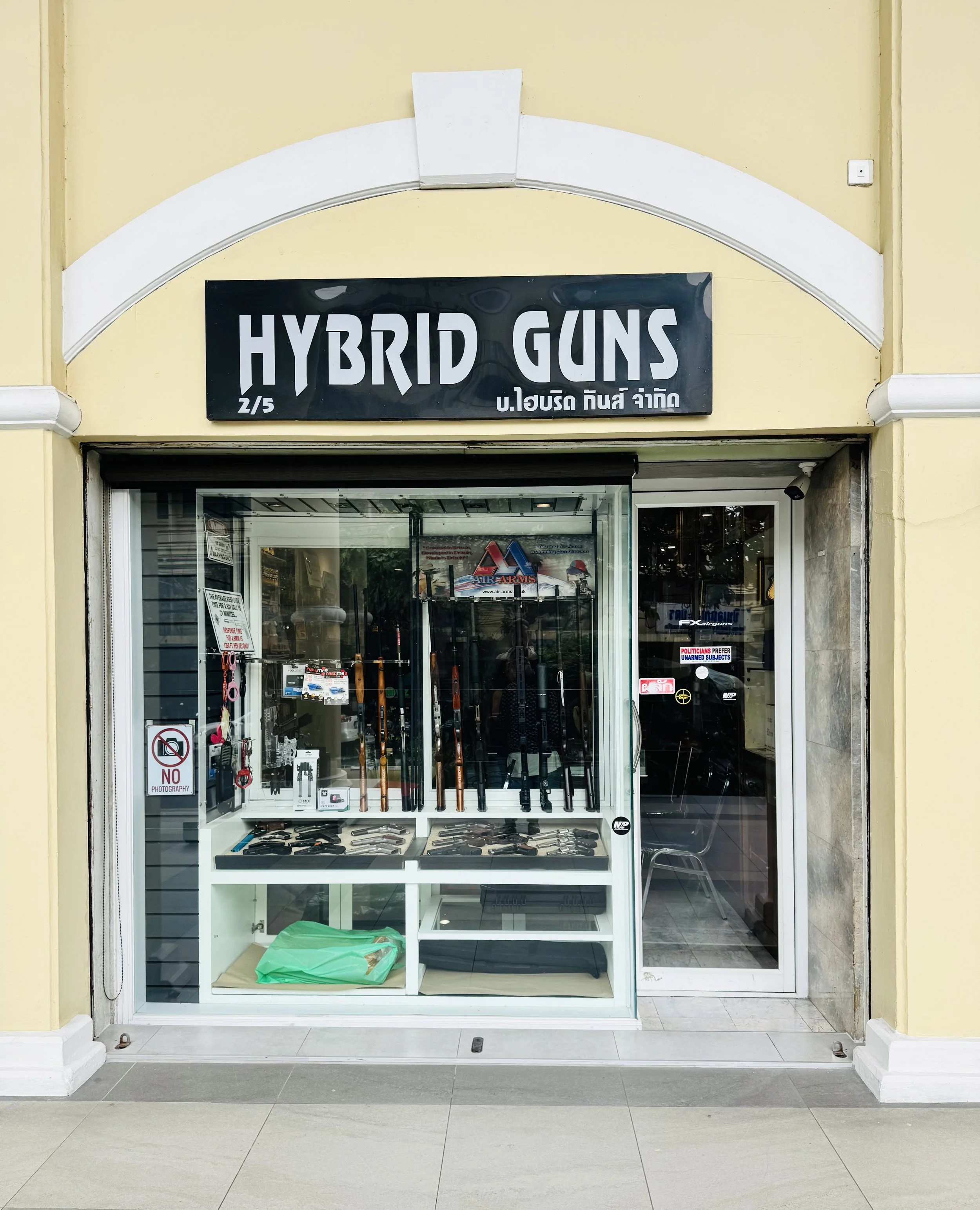 หน้าร้าน Hybrid Guns พร้อมป้ายชื่อร้านเหนือทางเข้ากระจก