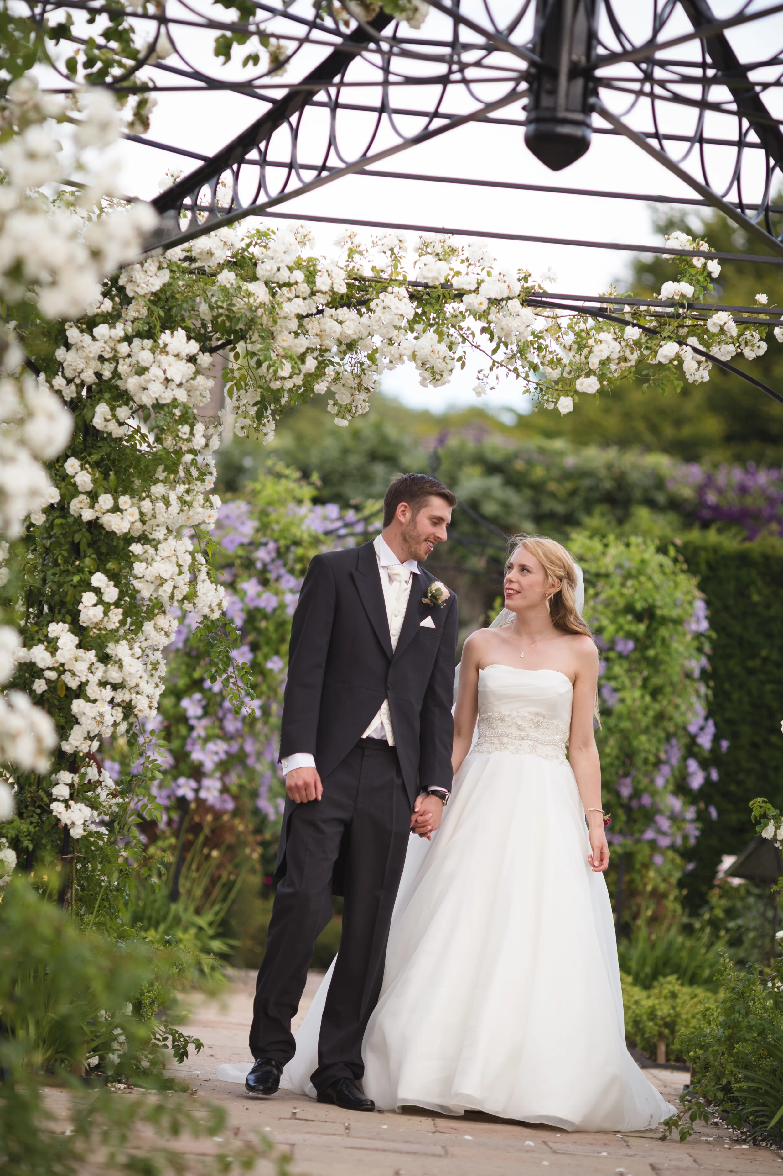 Bride and Groom walking under rose arbour