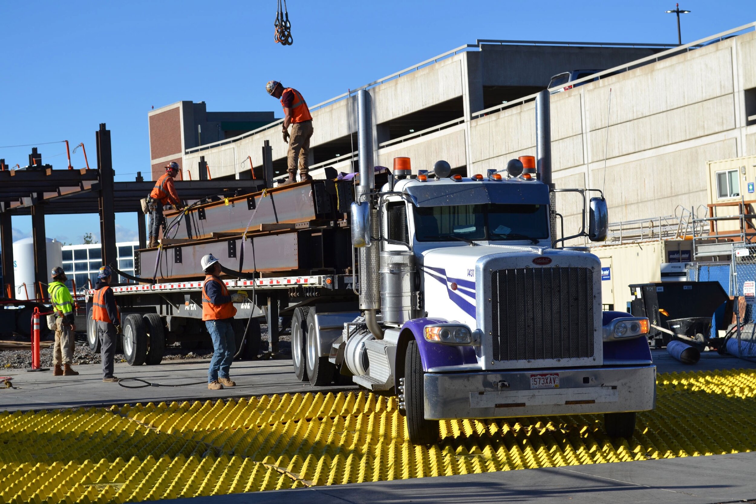 Workers unloading structural steel from delivery truck.