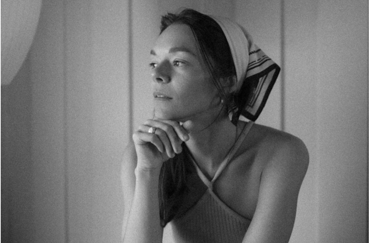 Woman in black jacket and lingerie, smiling, holding her hair.