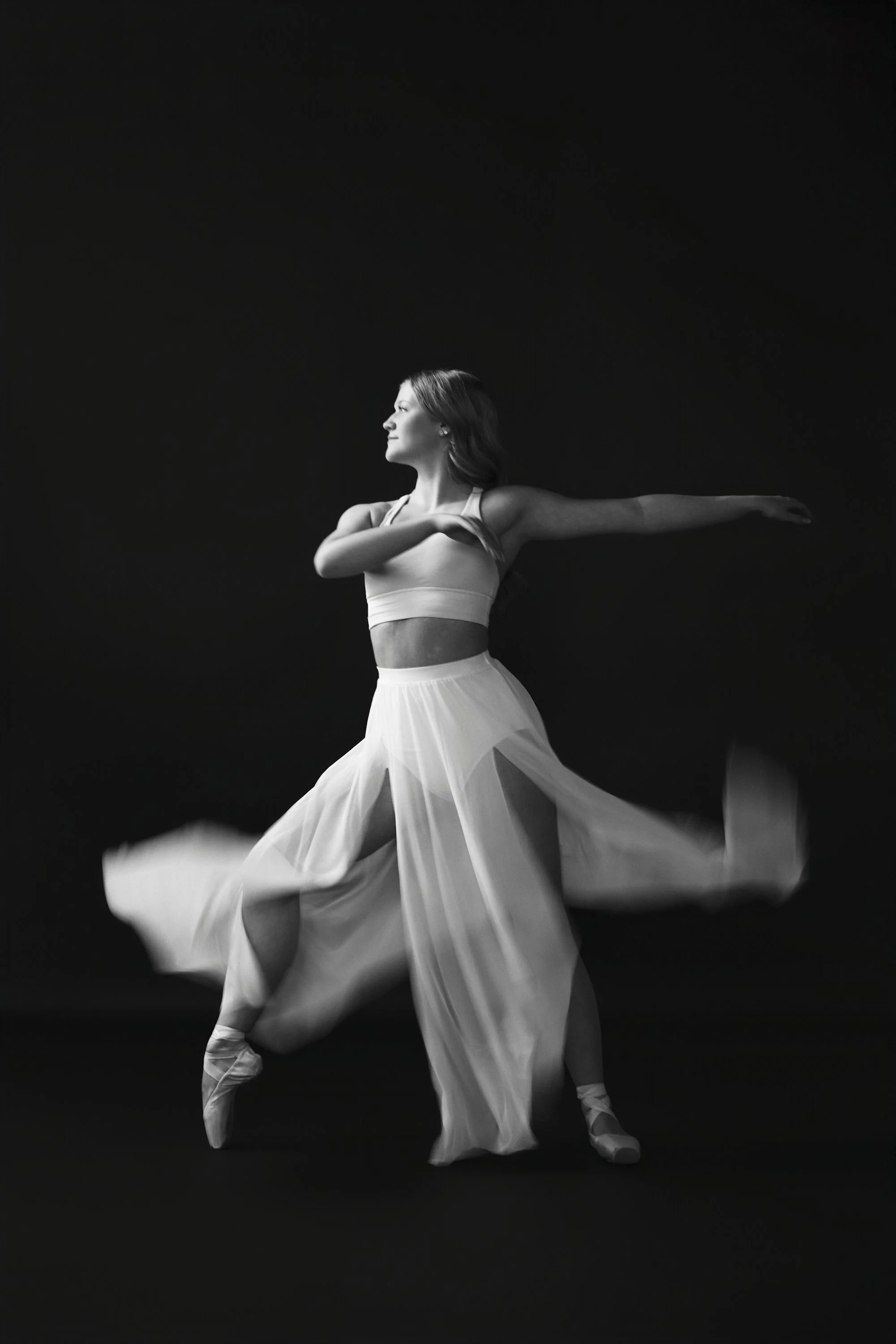 Dancer wearing pointe shoes in white skirt and top with black backdrop
