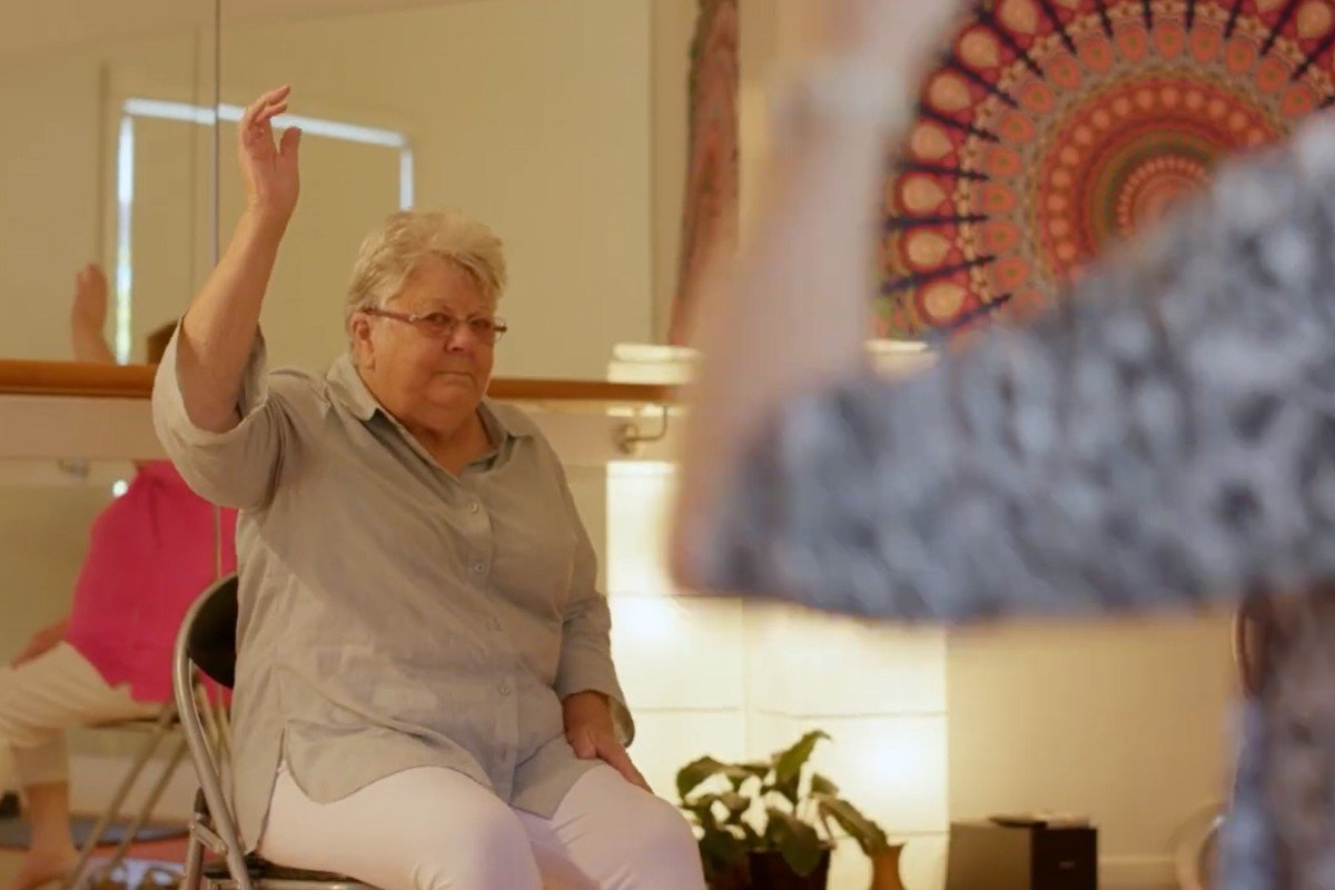 An over 60s woman in a grey shirt completes chair exercises during exercise classes for seniors in Adelaide.